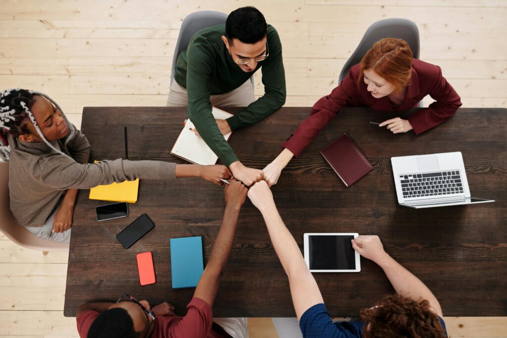A diverse group of people in a business meeting, showing teamwork with technology on a wooden table.